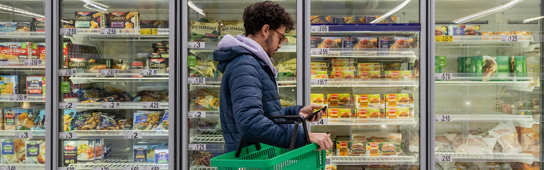 Man holding grocery cart in front of grocery refrigerators