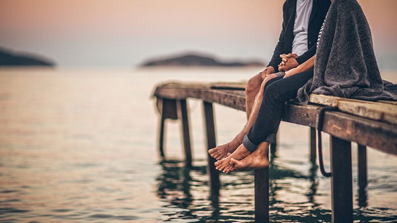 Couple sitting on a dock above water holding hands