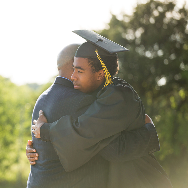 Graduating student in cap and gown hugging parent.